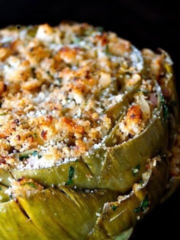 Very big stuffed artichoke that's golden on top, on a black background.